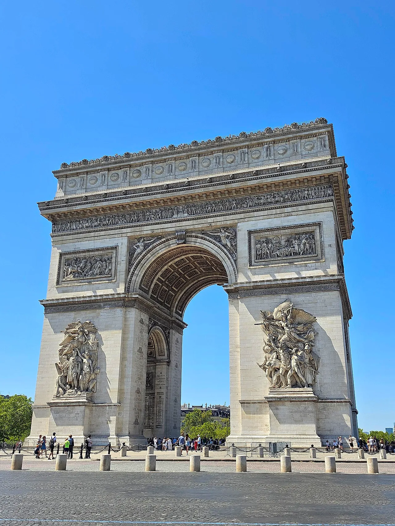 Close view of the Arc de Triomphe from below, showing the great sculpted group on the pier and the opening of the arch against a blue sky.