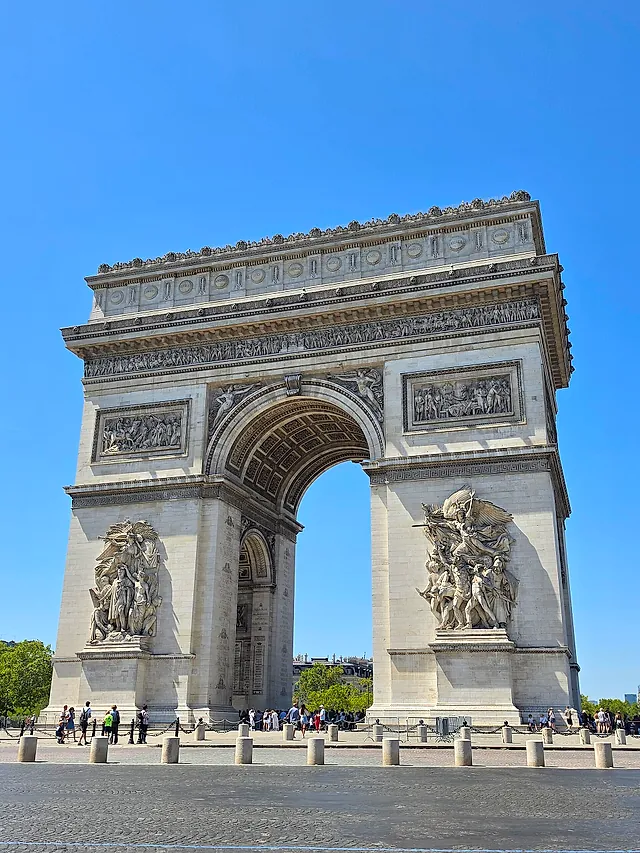 Close view of the Arc de Triomphe from below, showing the great sculpted group on the pier and the opening of the arch against a blue sky.