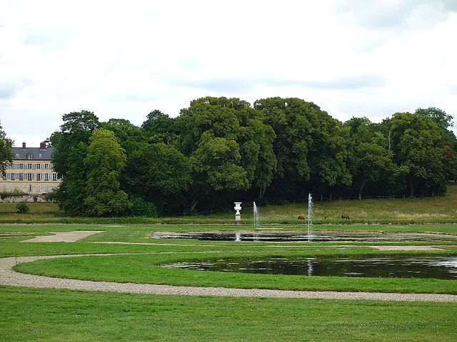The gardens of the Château de Chantilly: a wide lawn with a path, small jets of water in the pools and a dense line of trees behind.