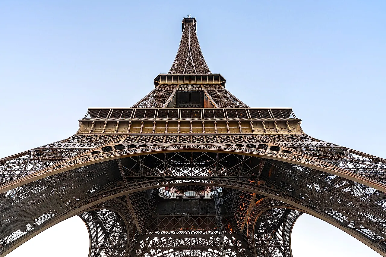 Looking up from under the Eiffel Tower: the four curving legs, the platforms and the slim upper section against the sky.