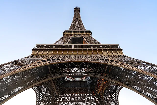 Looking up from under the Eiffel Tower: the four curving legs, the platforms and the slim upper section against the sky.