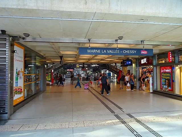 The concourse of Marne-la-Vallée–Chessy station, with the station name on a blue sign and travellers walking towards the exits.