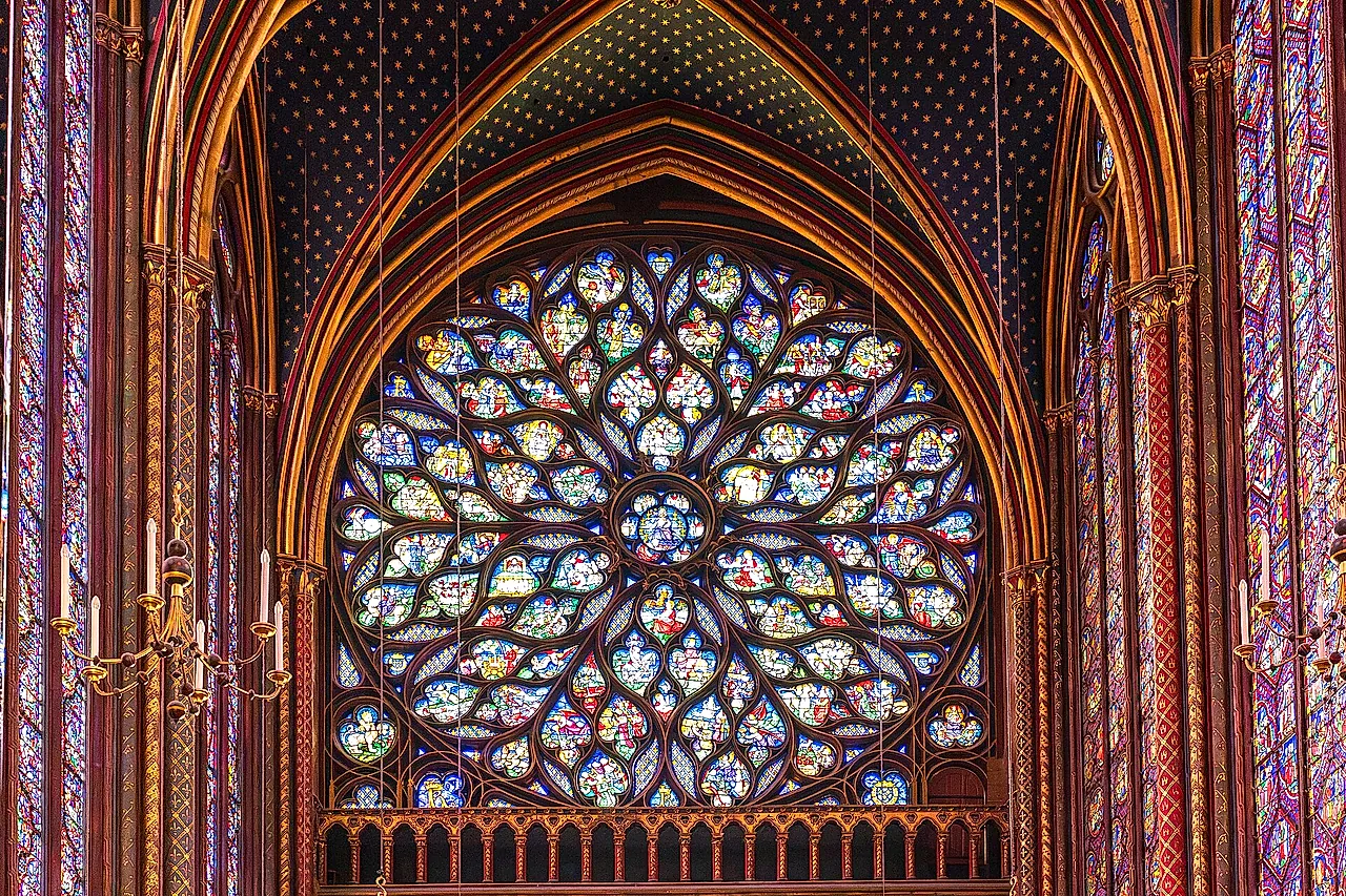 The great rose window of the Sainte-Chapelle glowing in red, blue and yellow glass, framed by painted stonework and tall lancet windows.