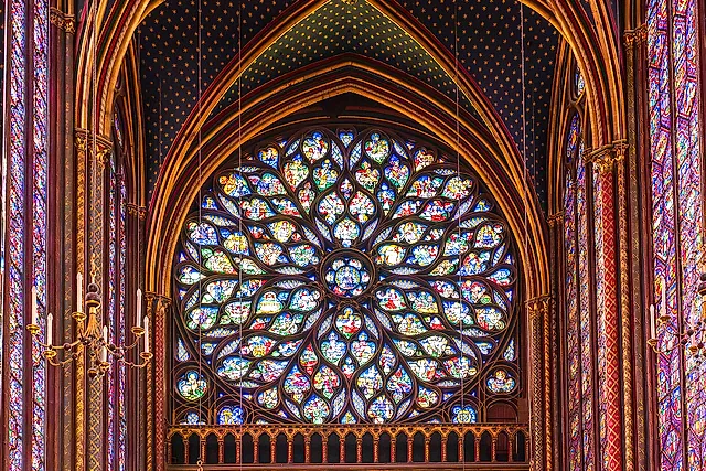 The great rose window of the Sainte-Chapelle glowing in red, blue and yellow glass, framed by painted stonework and tall lancet windows.