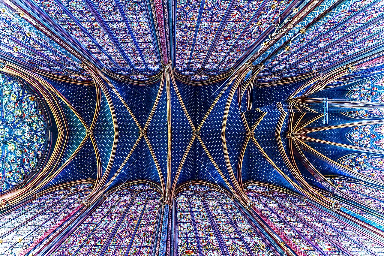 Looking straight up at the blue vault of the upper chapel of the Sainte-Chapelle, with gilded ribs and tall stained-glass windows around the edge.