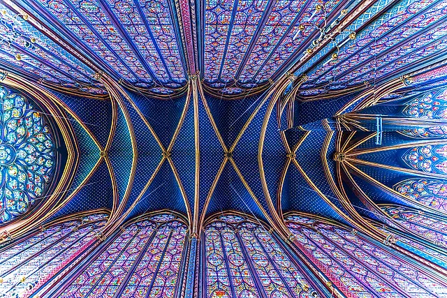 Looking straight up at the blue vault of the upper chapel of the Sainte-Chapelle, with gilded ribs and tall stained-glass windows around the edge.