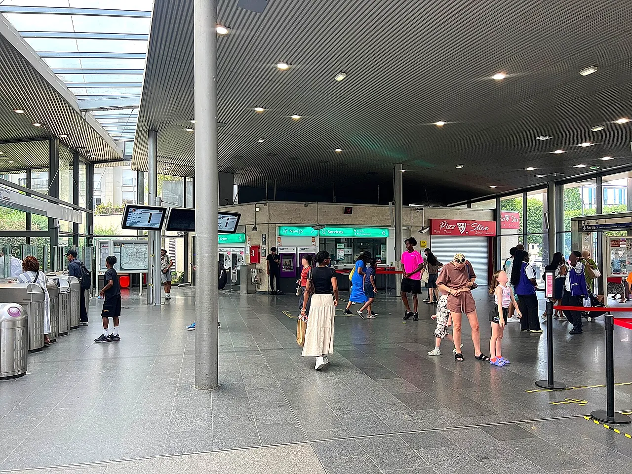 The ticket hall of Val d'Europe station with fare gates, information screens and a few travellers.
