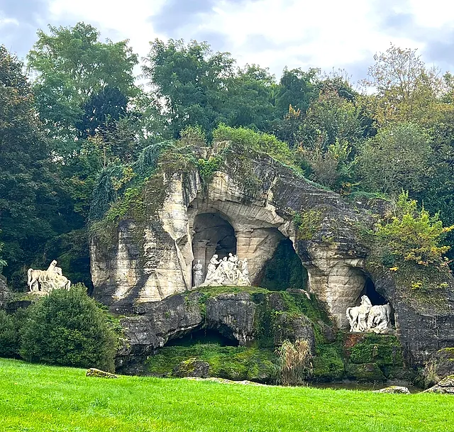 The Bosquet des Bains d'Apollon in the gardens of Versailles: an artificial rocky grotto covered in greenery, with white marble figures in its niches.